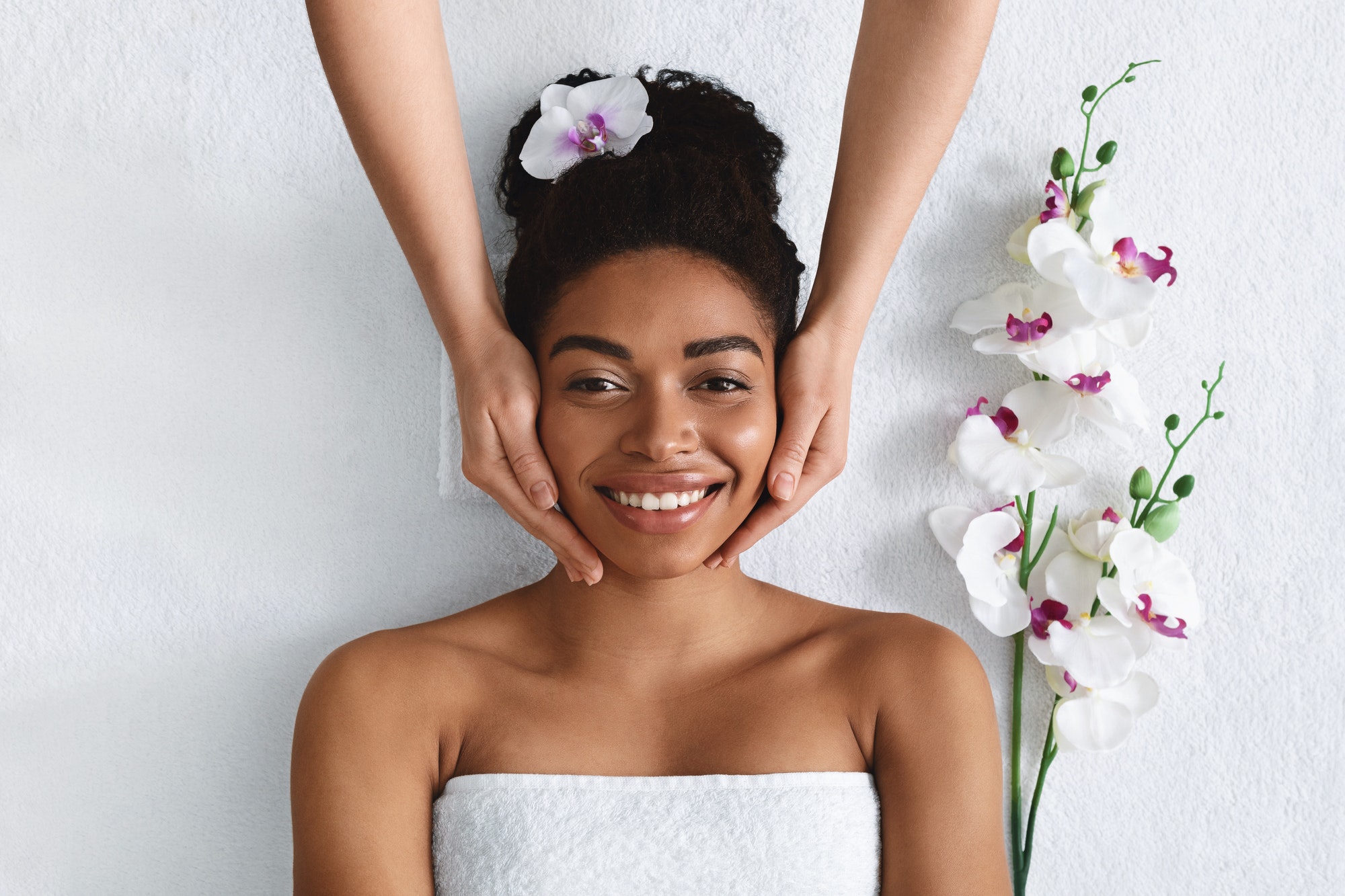 Beautician making face massage for happy black lady